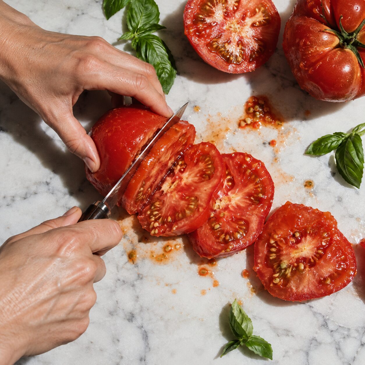 Hände schneiden Tomaten auf Marmor